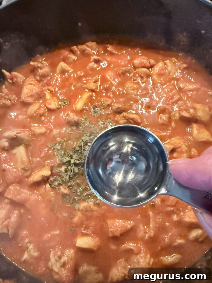 Kasuri methi (dried fenugreek leaves) and white vinegar being added to the simmering Chicken Jalfrezi, enhancing its aromatic profile.