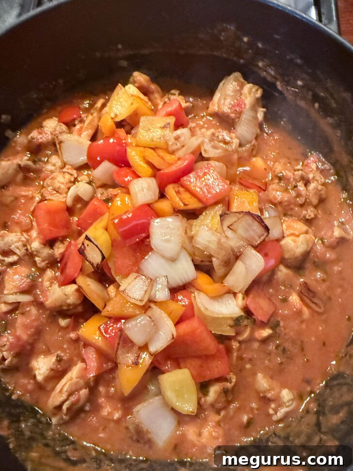 The vibrant, stir-fried bell peppers and onions being folded into the rich Chicken Jalfrezi curry, adding texture and color.