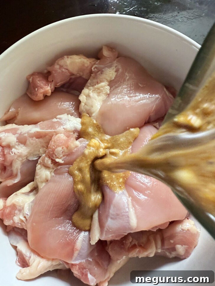 Pouring half of the fragrant marinade over boneless chicken thighs in a bowl.