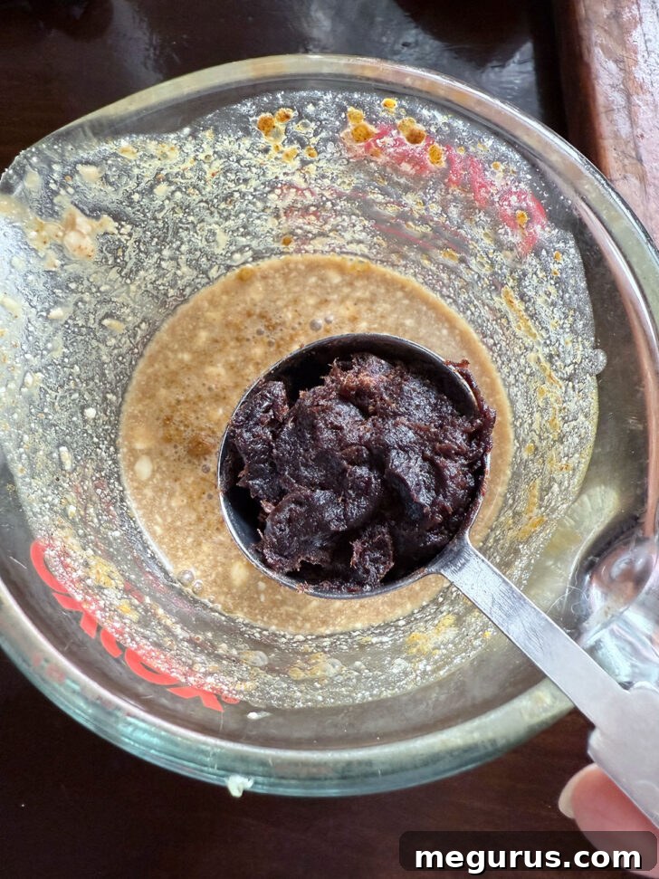 Adding rich tamarind paste to the reserved marinade, preparing it for the peanut sauce.