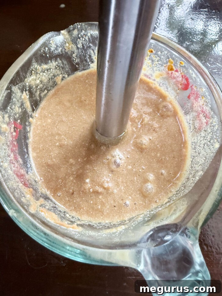 Blending the peanut sauce to a smooth, thick consistency using an immersion blender.
