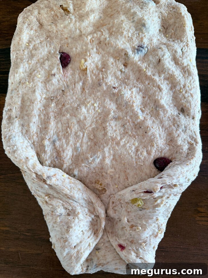 Folding the corners of the dough inwards before rolling to shape the loaf.