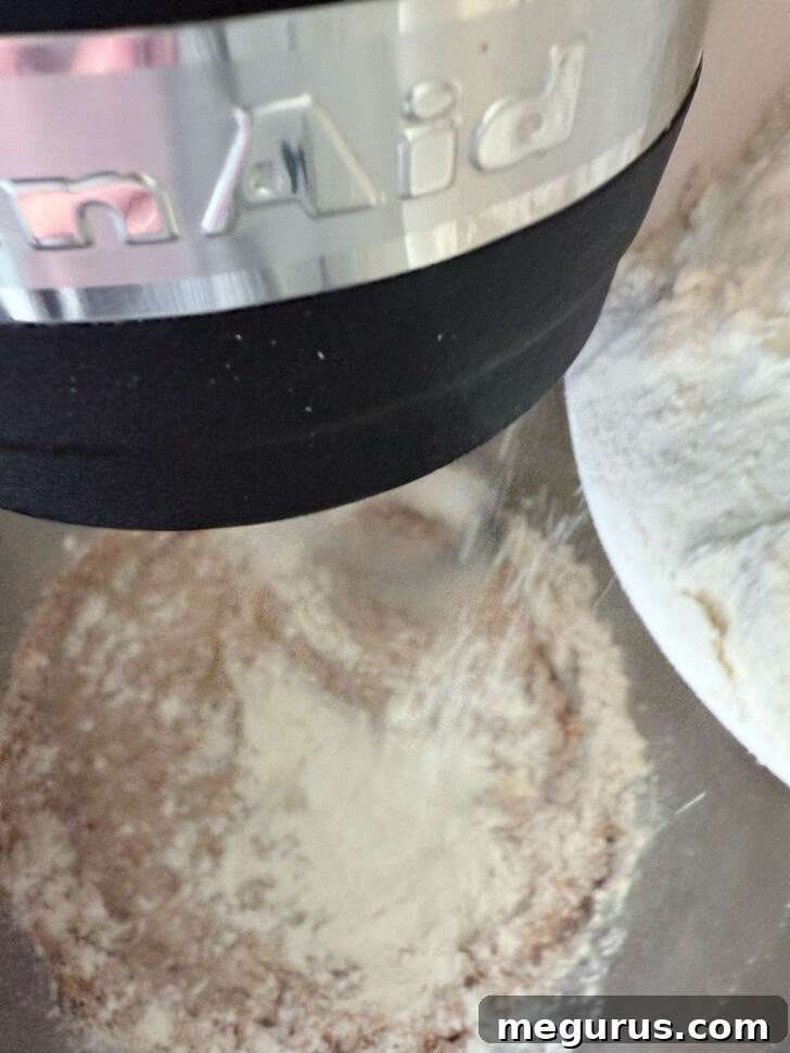 Gradually adding all-purpose flour to the mixing bowl to form the dough.