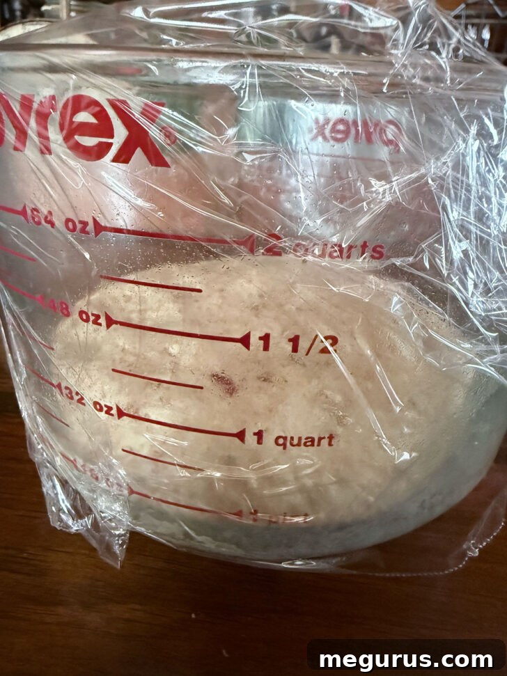 Dough set to rise in a large measuring cup, covered with plastic wrap.