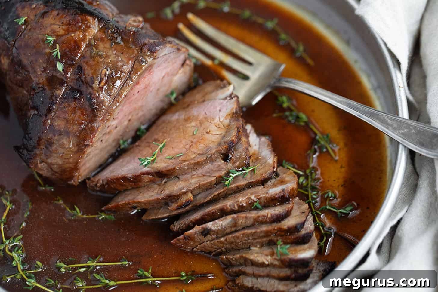 Herb mustard roast beef sliced in serving dish with gravy.