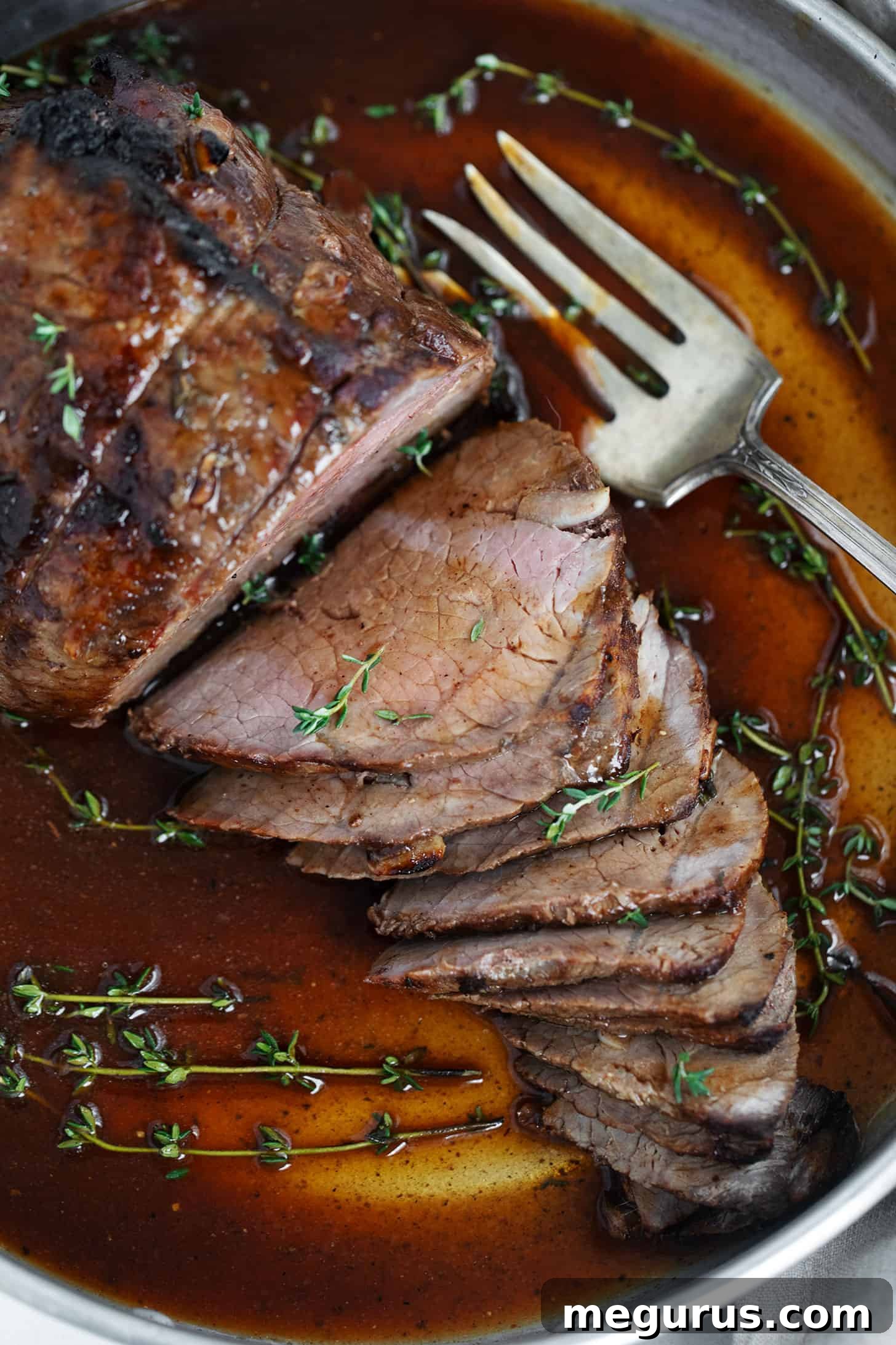 Herb mustard roast beef sliced in serving dish with gravy.