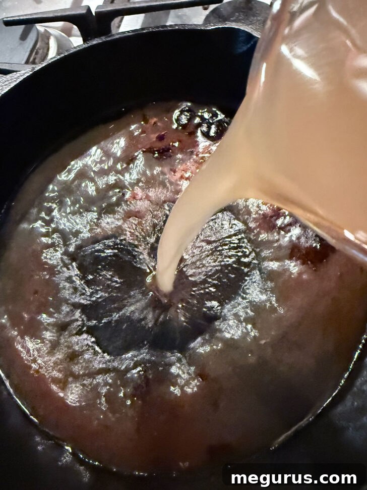 Adding broth the drippings in the cast iron skillet.