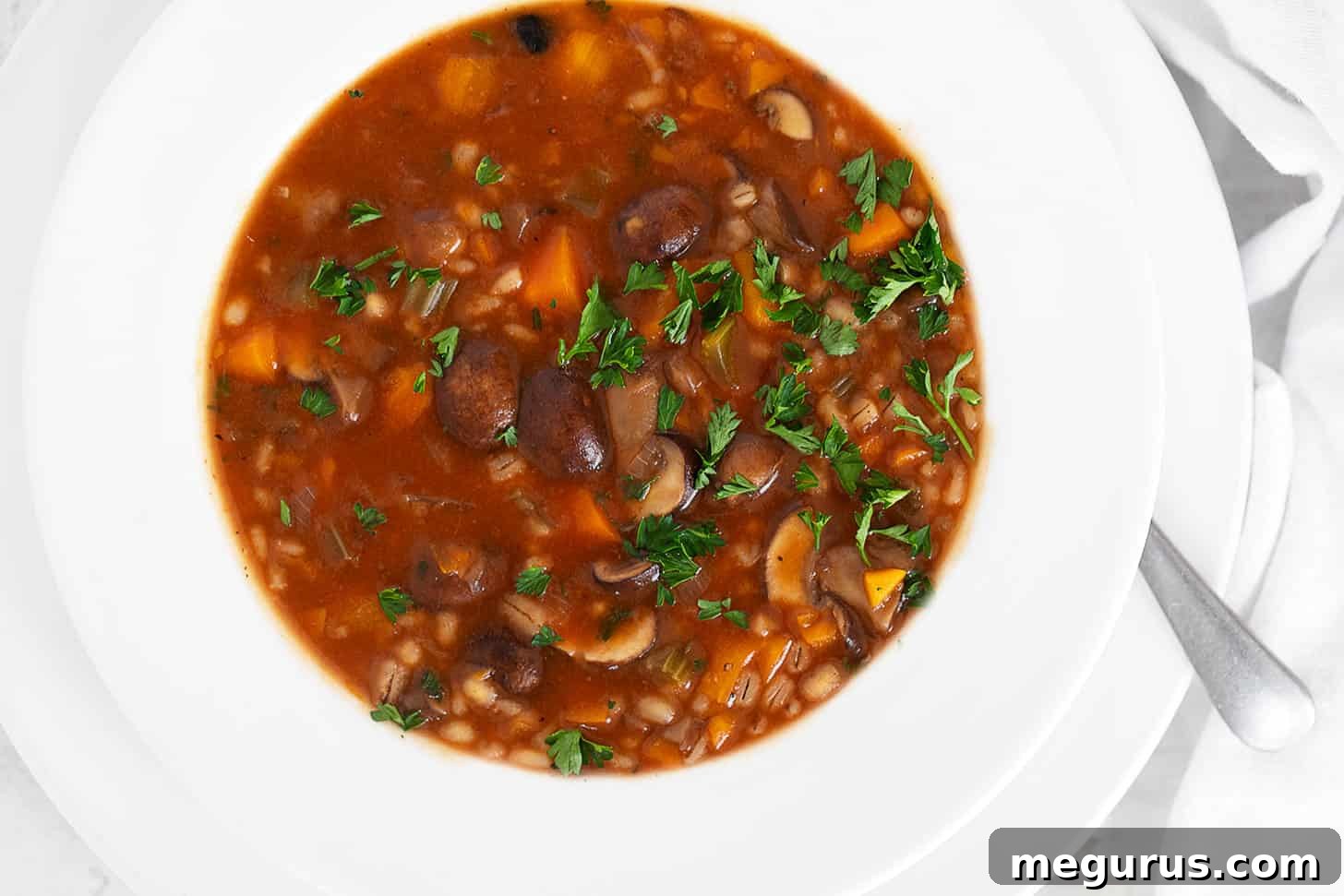 A steaming bowl of hearty Mushroom Barley Soup, garnished with fresh parsley.