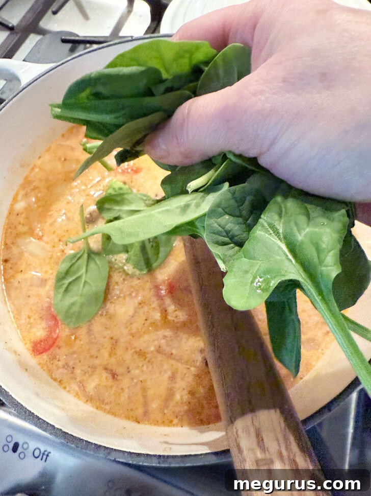 Baby spinach being added to the simmering soup broth in the pot.