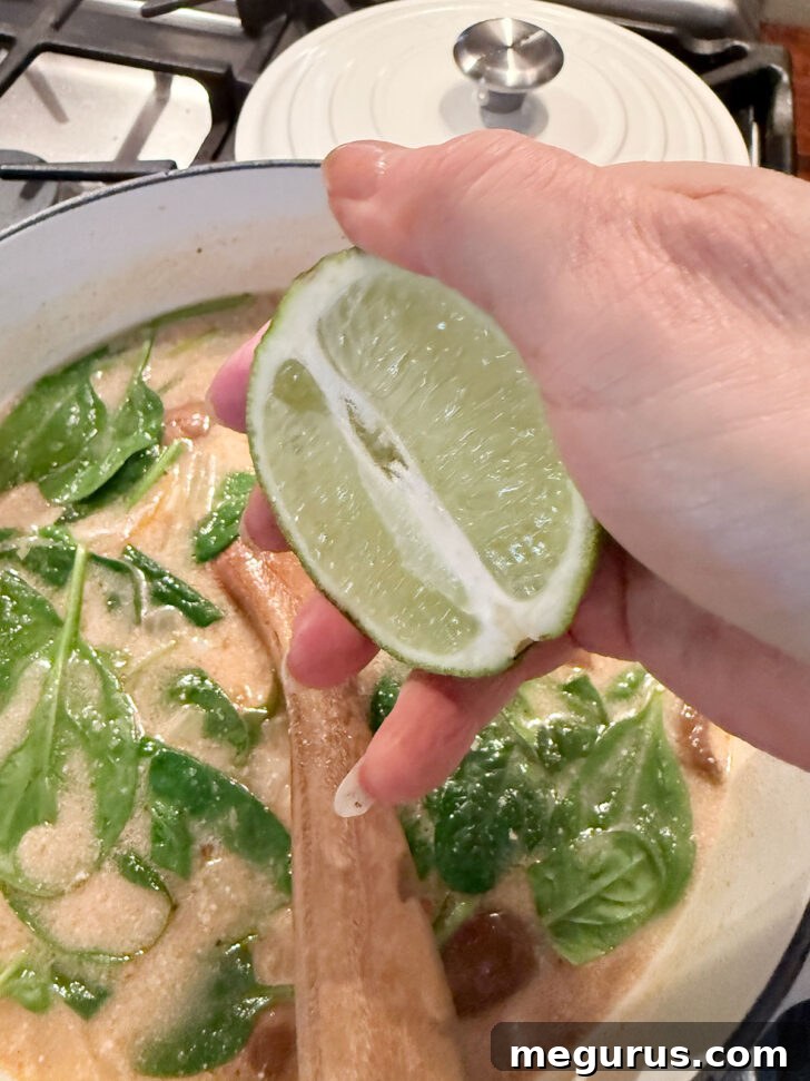 A lime half being squeezed over the spicy coconut ramen in the soup pot.