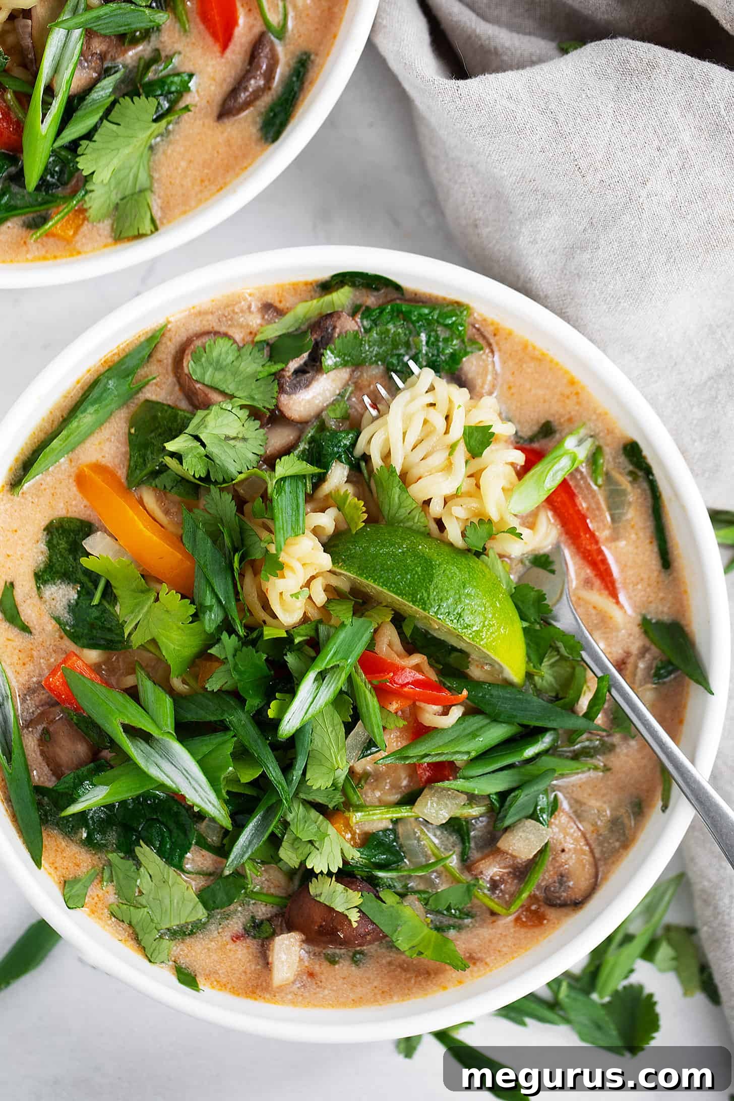Two bowls of spicy coconut ramen, garnished with green onions and cilantro, with a fork in one bowl.