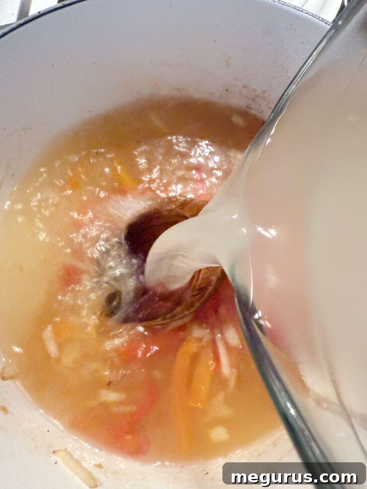 Chicken broth being poured into the soup pot with the cooked aromatics.
