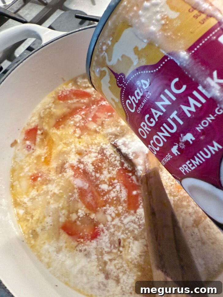 A can of coconut milk being added to the simmering soup broth.