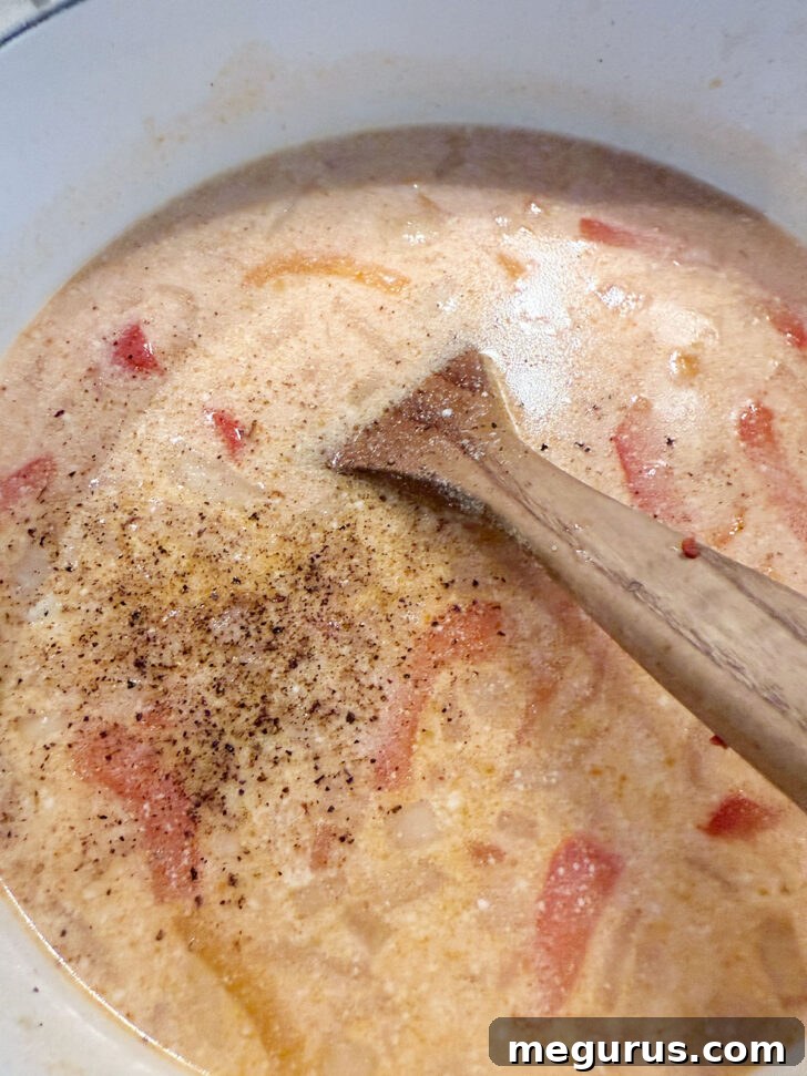 A hand seasoning the soup with salt and freshly ground pepper.