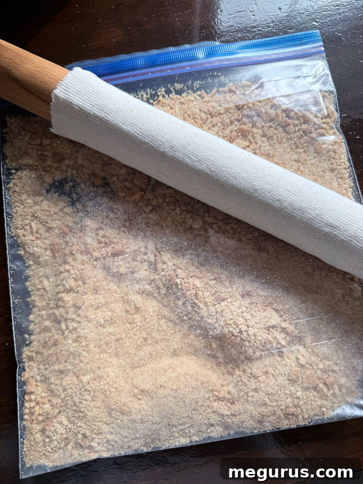 A rolling pin being used to crush Digestive biscuits inside a plastic zipper bag on a flat surface, illustrating the preparation of the base.