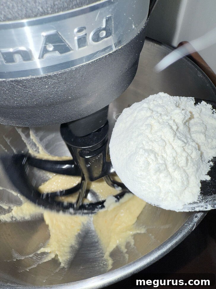 The process of gently adding the dry flour mixture into the wet batter inside a stand mixer, ensuring even incorporation.