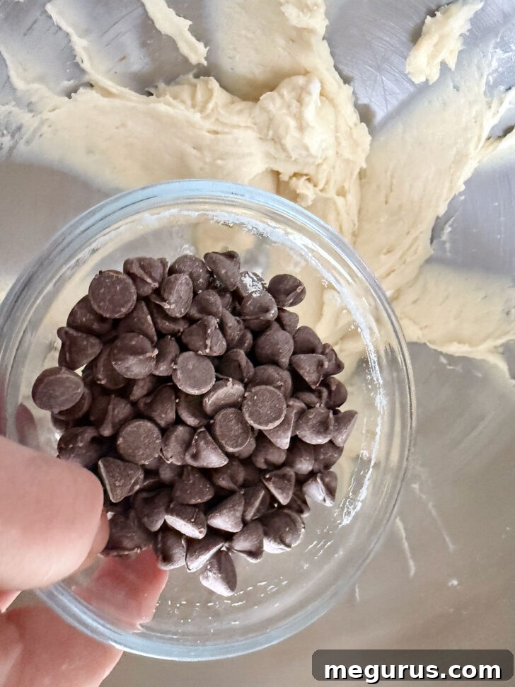 Close-up shot of chocolate chips being folded into the coffee cake batter using a rubber spatula, ensuring even distribution.