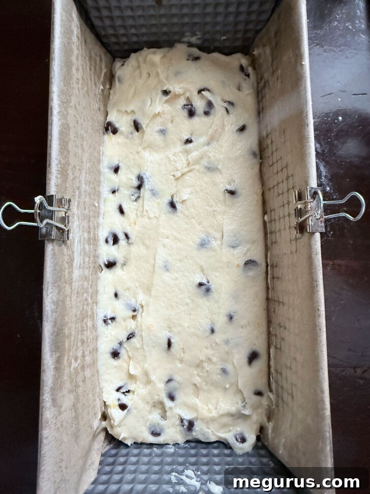 The prepared coffee cake batter evenly spread into a parchment-lined loaf pan, ready for the final touches before baking.