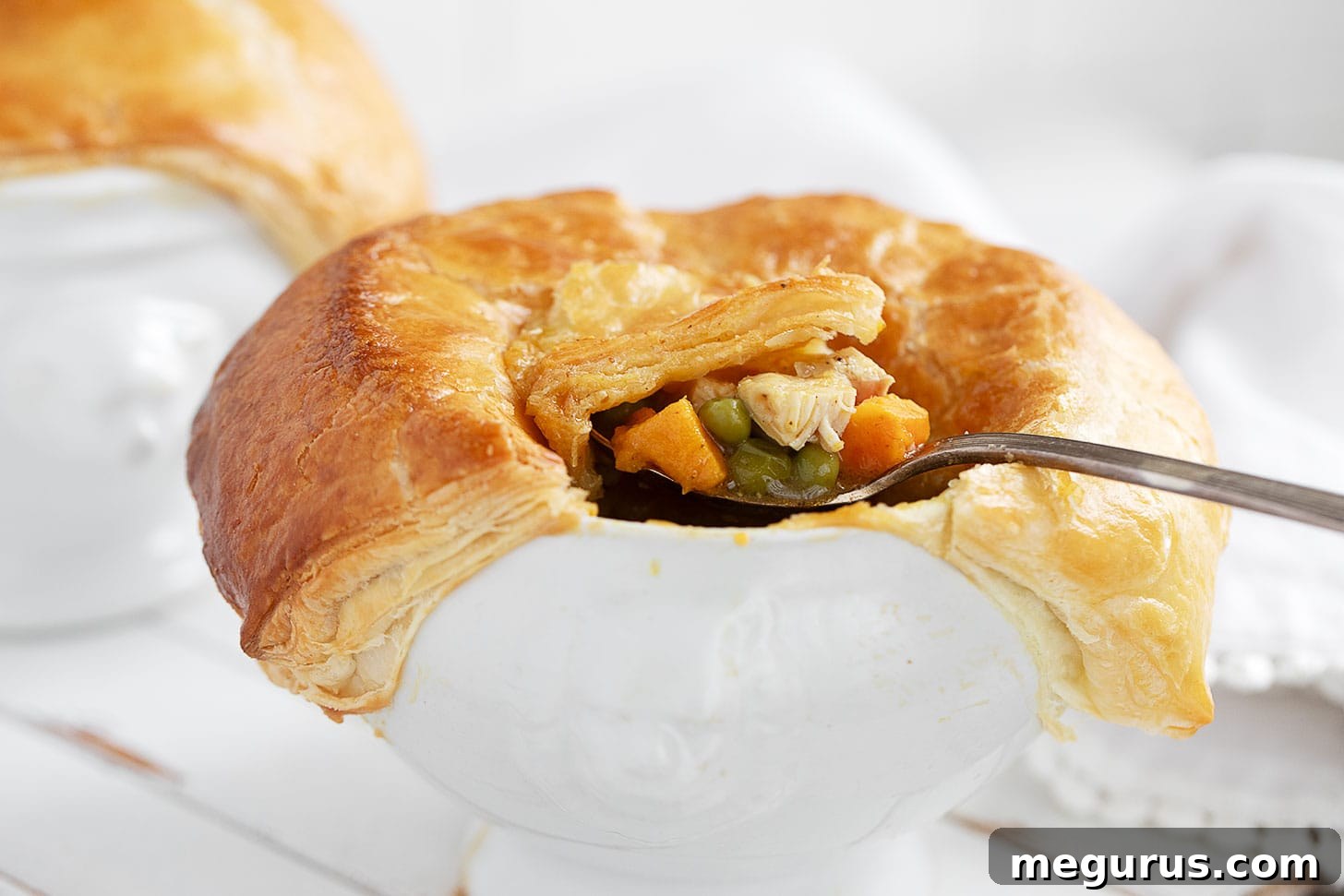Curried chicken pot pie in baking dish with spoon, golden-brown puff pastry.