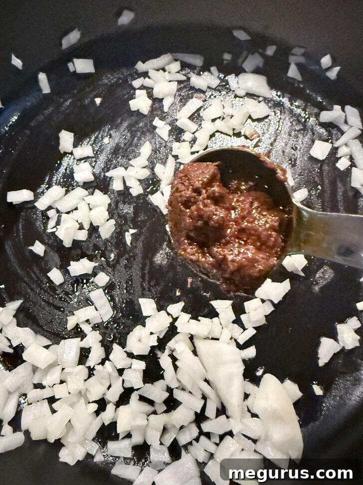 Adding Madras curry past to cooked onions, illustrating the first step of building flavor.