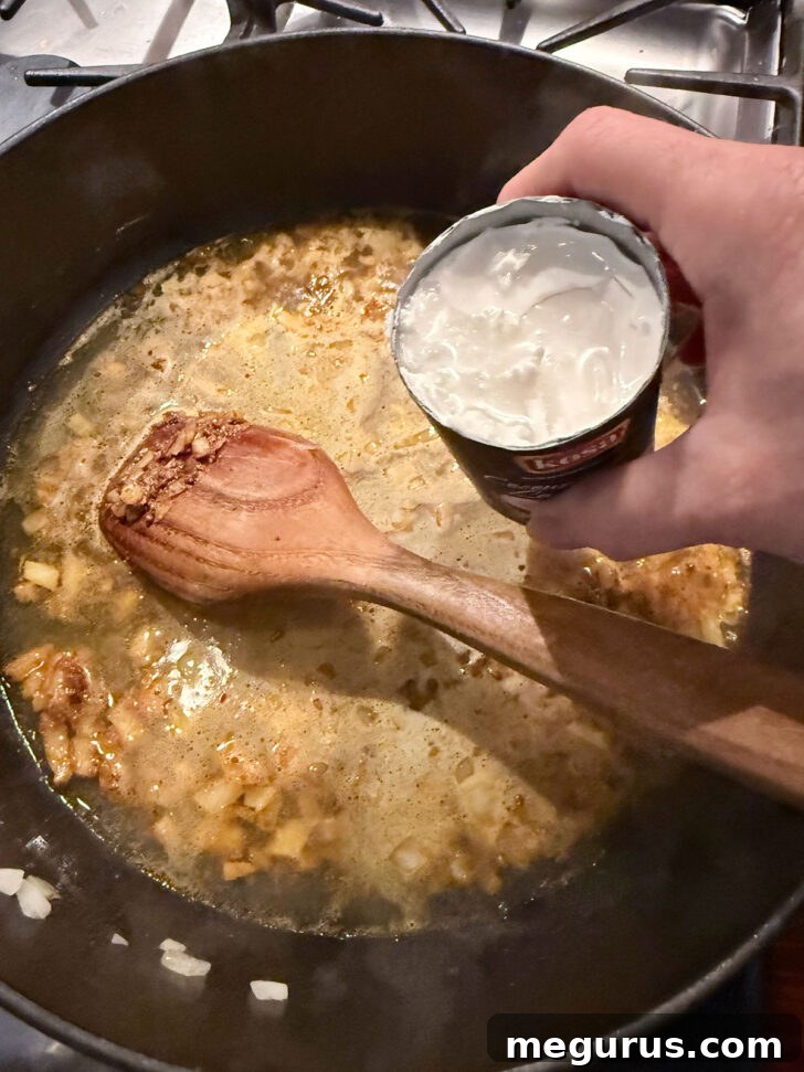Adding coconut milk to the simmering chicken broth and curry mixture in the skillet.
