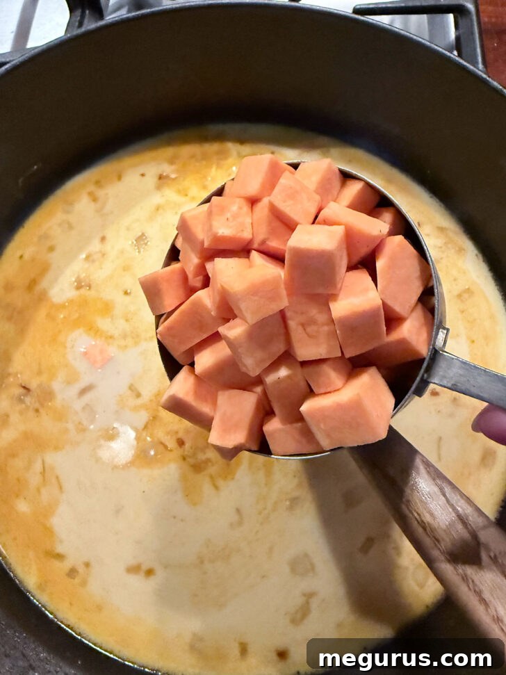 Adding diced sweet potato to the simmering curry mixture in the skillet.