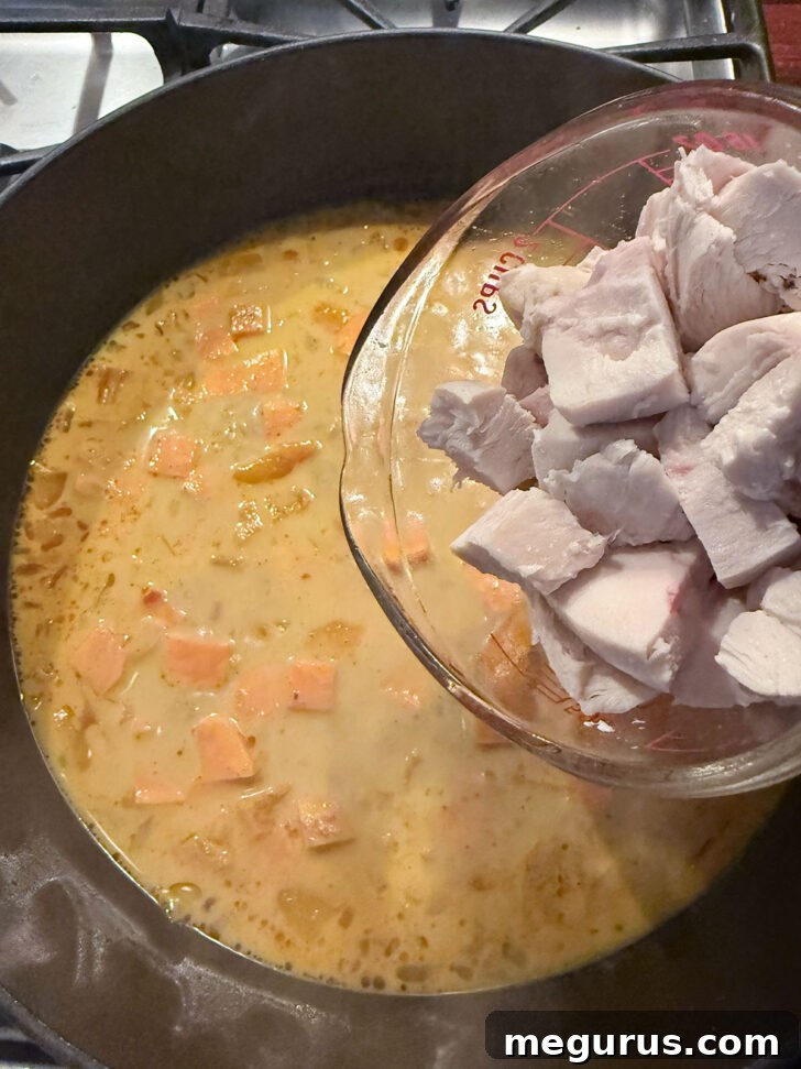 Adding cooked and diced chicken to the skillet, ready to be integrated into the filling.