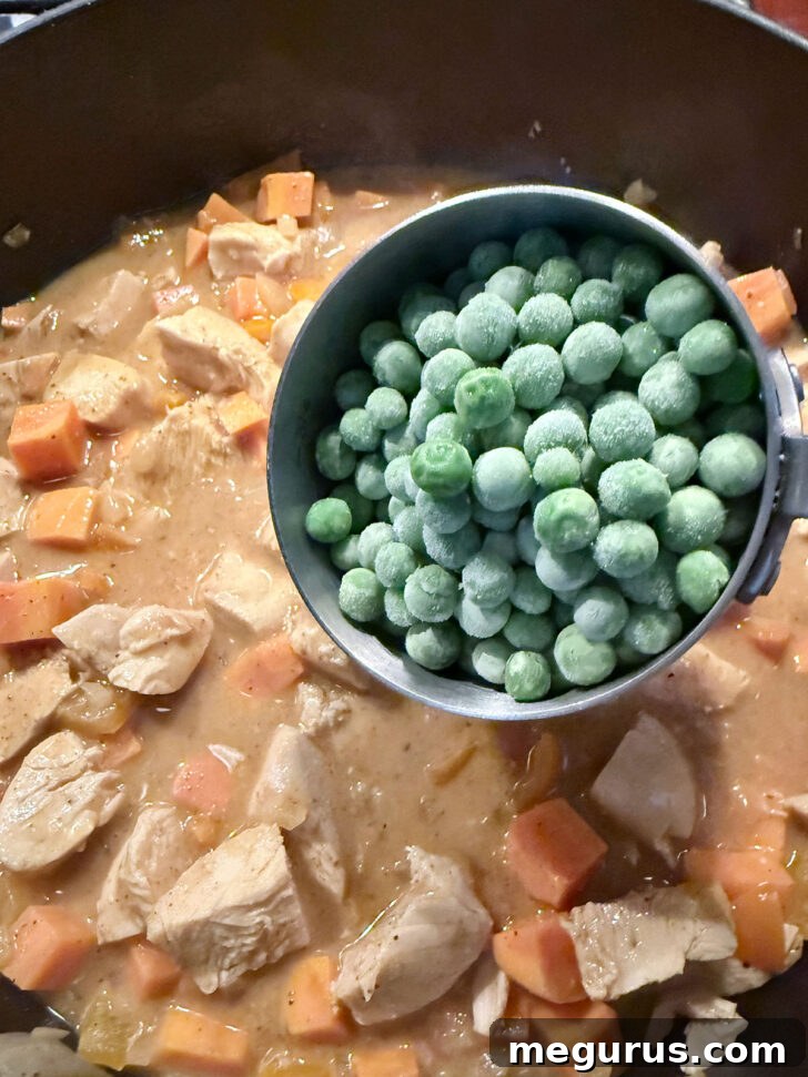 Adding frozen peas to the skillet, adding a final vegetable component.