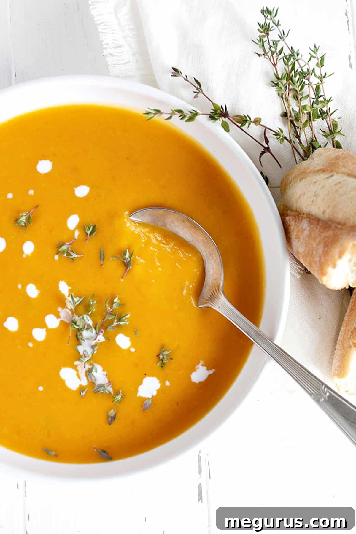 Close-up of creamy butternut squash soup in a white bowl, garnished with cream swirls and fresh thyme