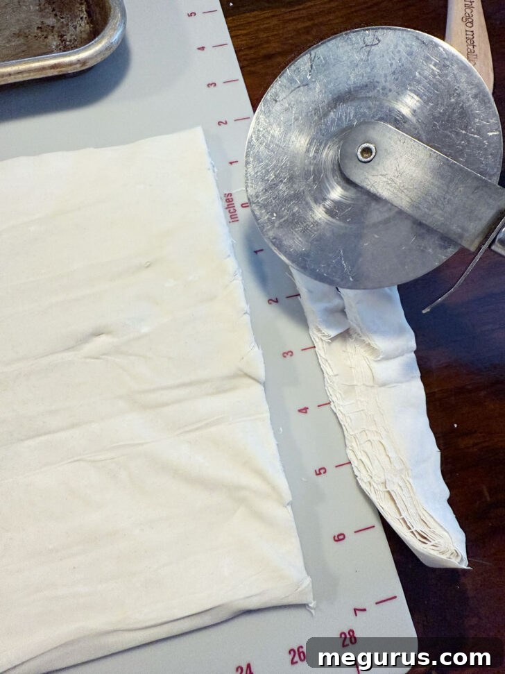 Trimming the phyllo pastry with a pizza cutter to fit the baking pan.
