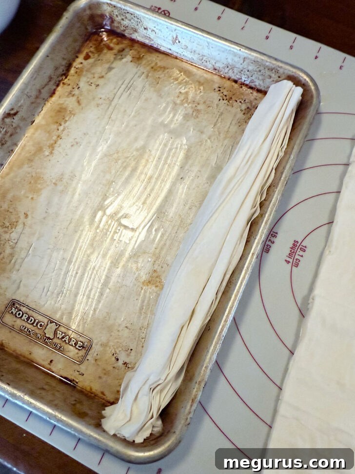 Accordion-folded phyllo pastry sheets being arranged onto a buttered baking sheet.