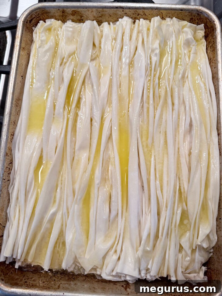 Melted butter being generously poured over the partially baked, crinkled phyllo pastry.