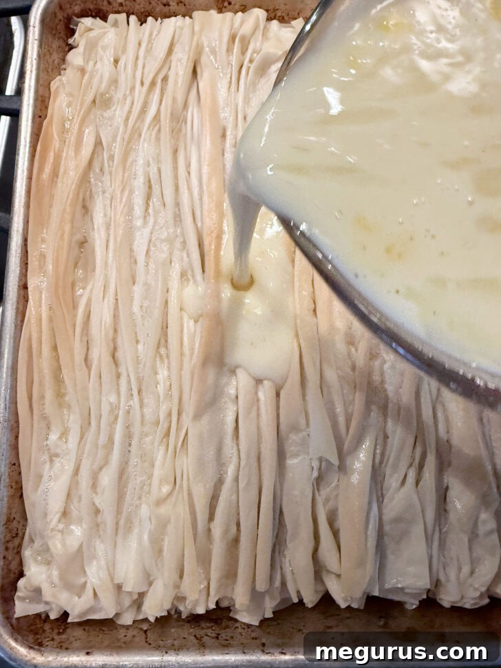 The creamy custard mixture being evenly poured over the butter-drizzled phyllo pastry.