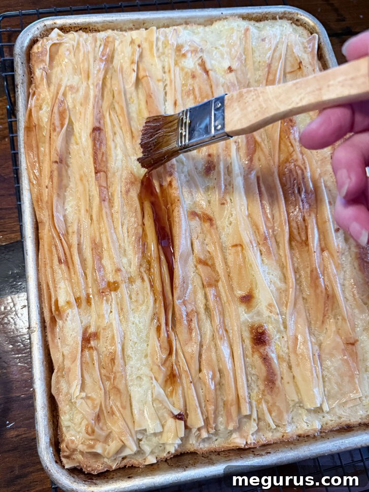 Freshly baked phyllo crinkle cake being generously brushed with maple syrup.