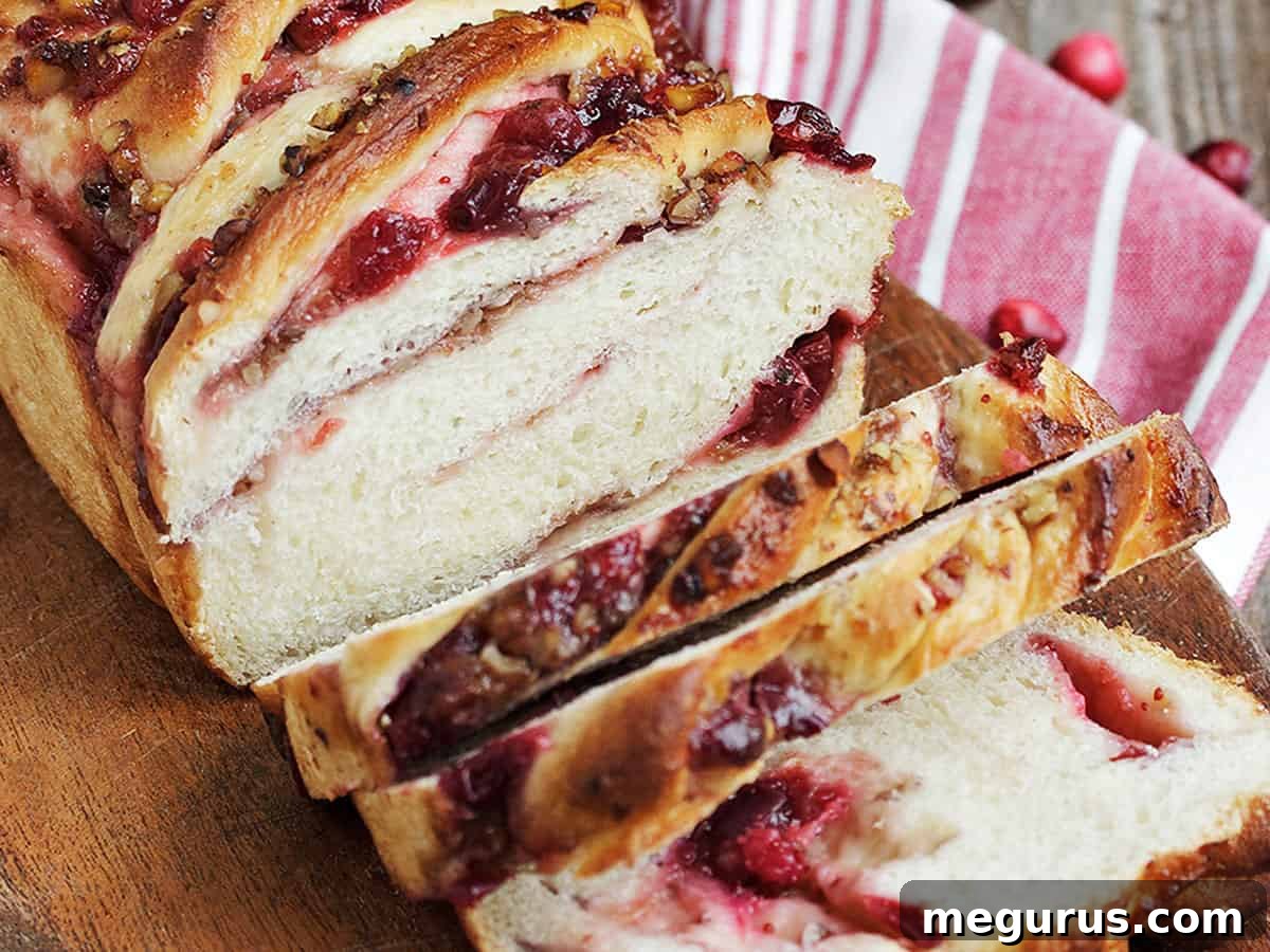 A close-up of freshly sliced cranberry walnut swirl bread, showing the rich red swirl of cranberry and scattered walnuts.