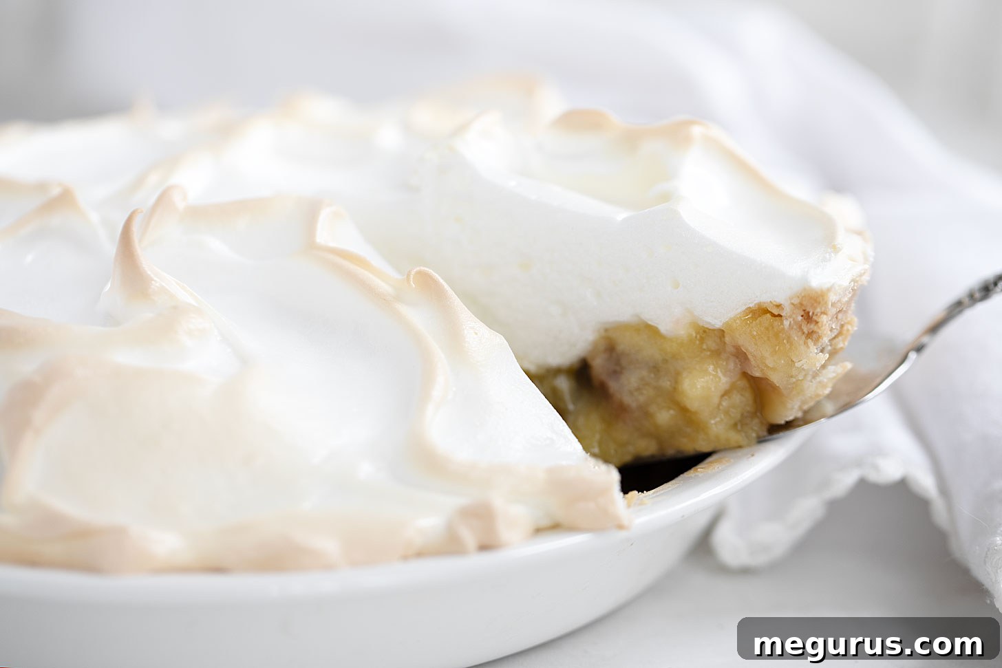 A perfectly sliced Rhubarb Meringue Pie, showcasing its vibrant rhubarb custard and lofty white meringue topping, resting in a ceramic pie dish.