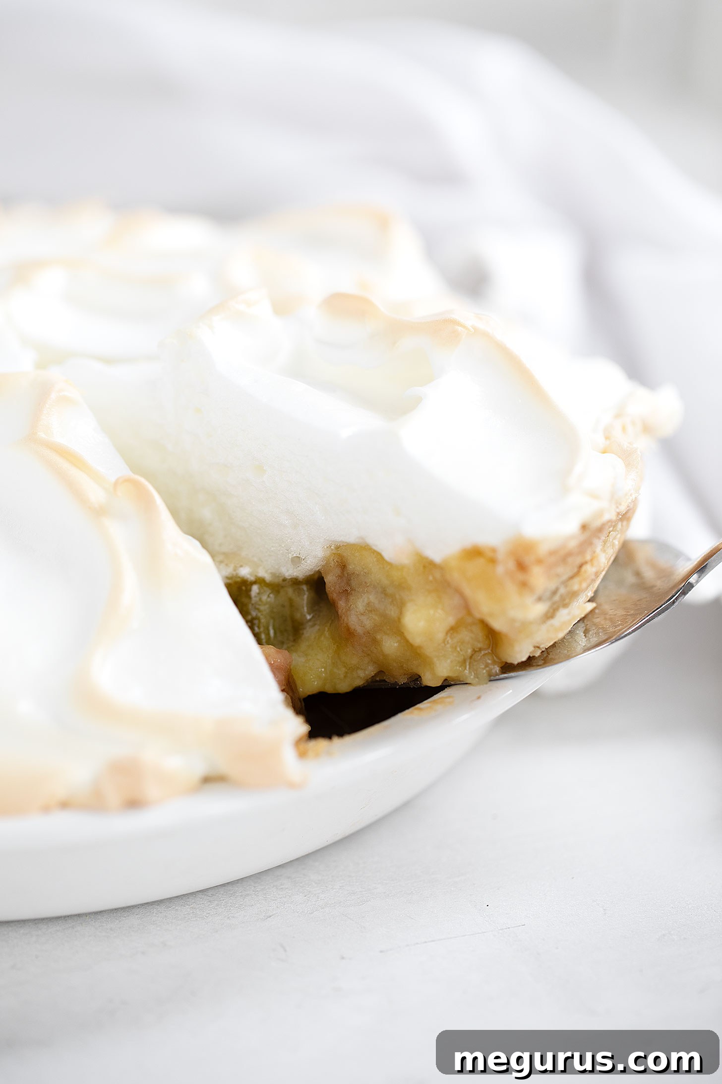 A close-up view of a slice of Rhubarb Meringue Pie, revealing the tender rhubarb custard and the fluffy, golden-tipped meringue.