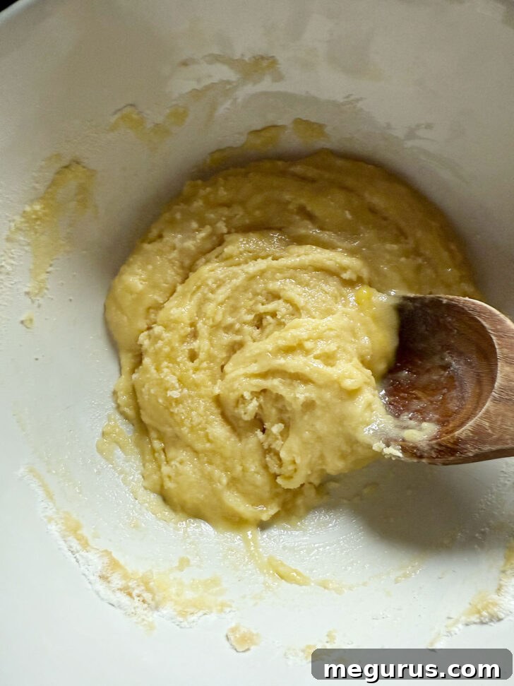 A thick mixture of eggs, flour, and sugar stirred together in a bowl, forming the custard base before rhubarb is added.