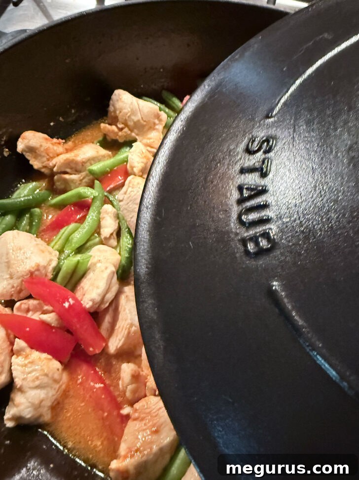 The skillet is covered, allowing the vegetables to gently simmer and soften in the rich curry base.