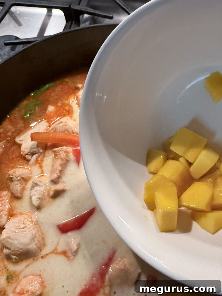 Adding a generous portion of fresh, diced mango to the simmering curry, enhancing its sweetness and texture.