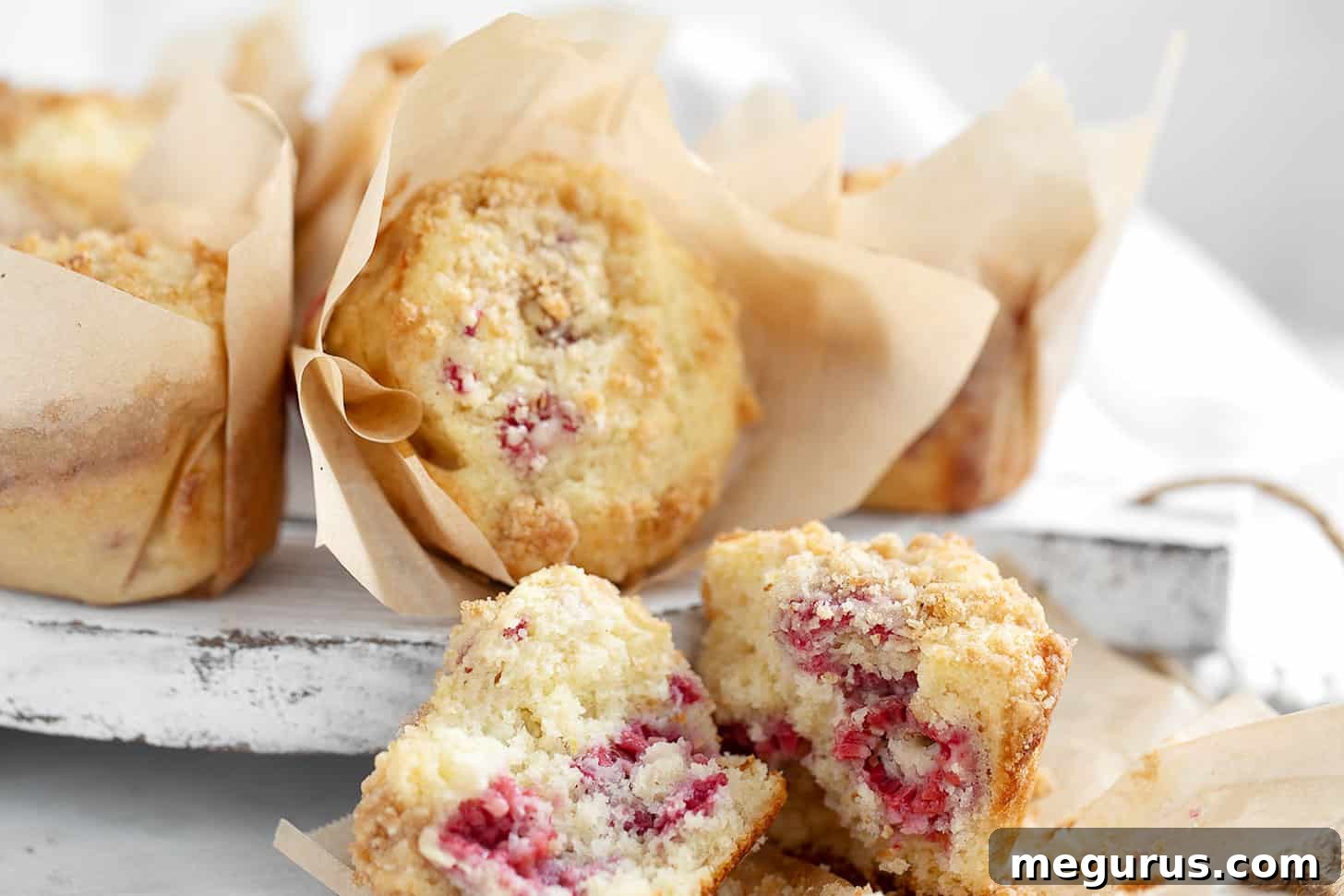 Raspberry lemon muffins on serving board, beautifully golden with a crumb topping.