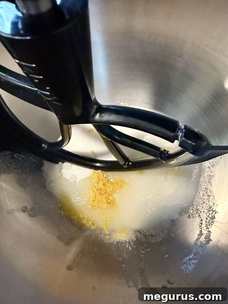 Sugar, lemon juice, and lemon zest in a stand mixer bowl, ready to be mixed.
