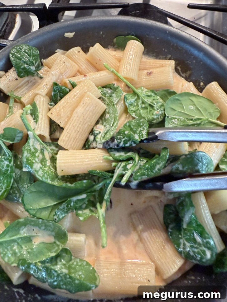 Cooking the spinach with the pasta in the skillet.