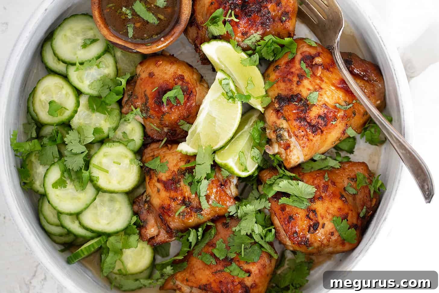 Vietnamese chicken thighs in serving dish with fresh cucumber salad, garnished with lime and cilantro.