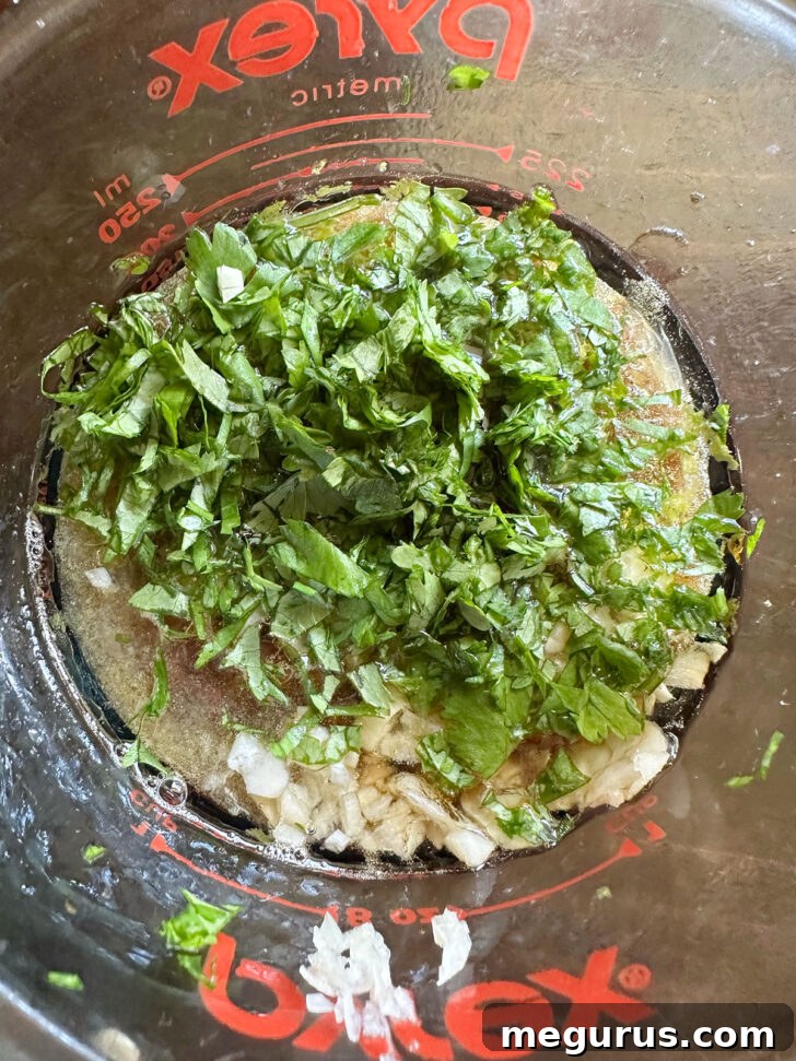 Vietnamese chicken marinade ingredients in a measuring cup, showcasing rich liquid and fresh herbs.