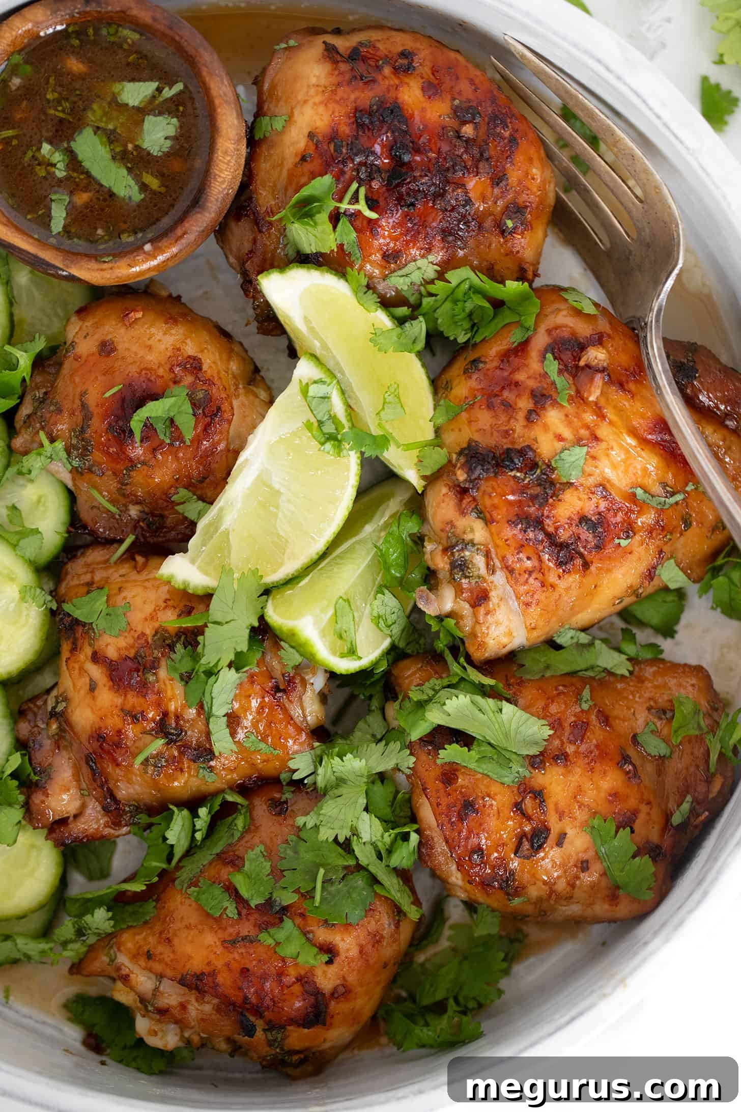 Close-up of Vietnamese chicken thighs in a serving dish, garnished with fresh herbs and served with a vibrant pickled cucumber salad, showcasing a complete and appealing meal.