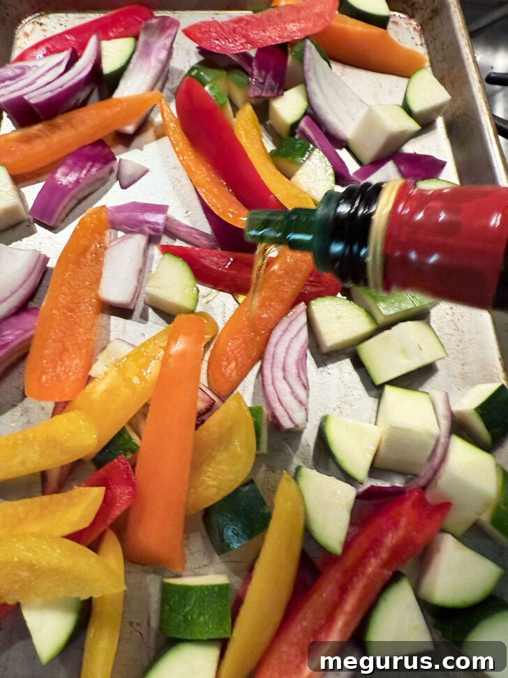 Drizzling olive oil over cut vegetables on a baking sheet before roasting.