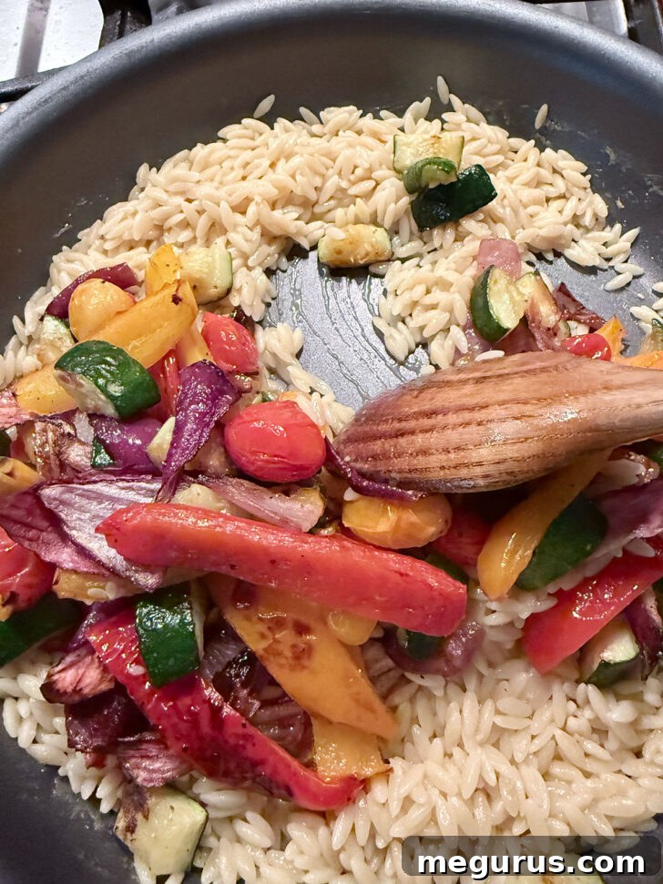 Adding the roasted vegetables to the skillet with the cooked orzo.