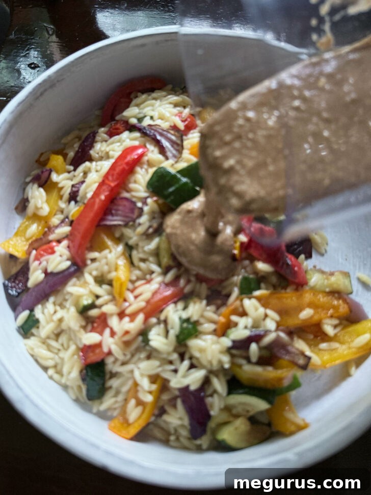 Adding the balsamic dressing to the orzo and roasted vegetables in a serving bowl.