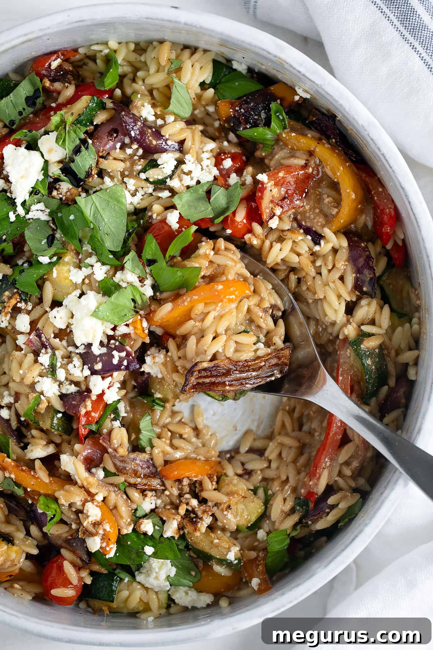 Close-up of roasted vegetable orzo in a serving dish with a spoon.